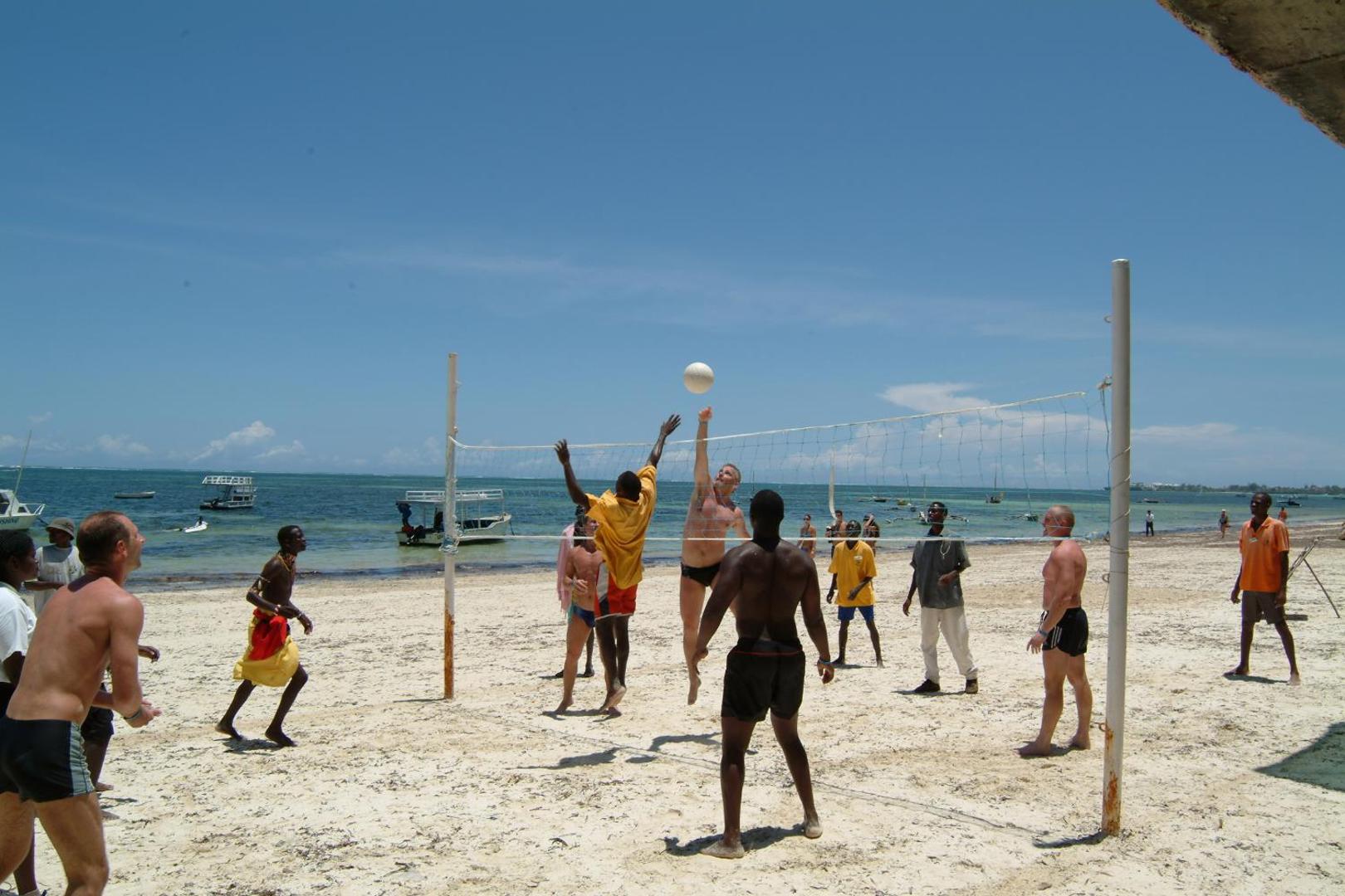 Viesnīcas viesi spēlē pludmales volejbolu Bamburi Beach Hotel baltajās smiltīs pie Indijas okeāna saulainā dienā.