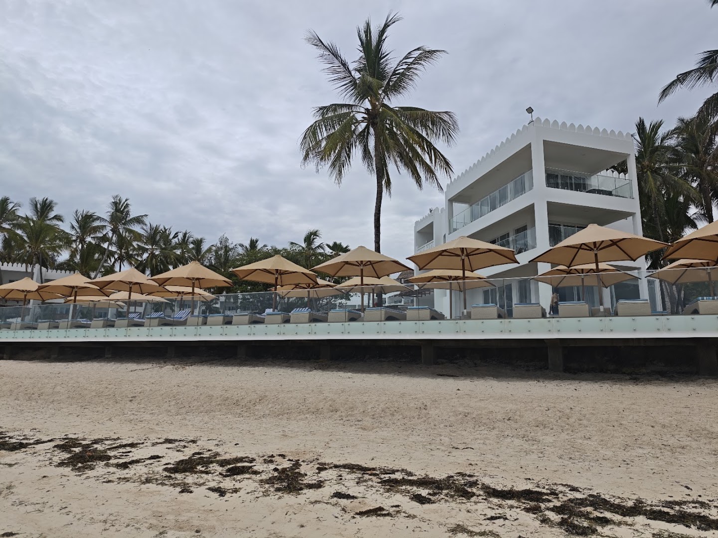 Bamburi Beach Hotel modernā korpusa fasāde ar balkoniem un sauļošanās zonu zem saulessargiem pludmales krastā