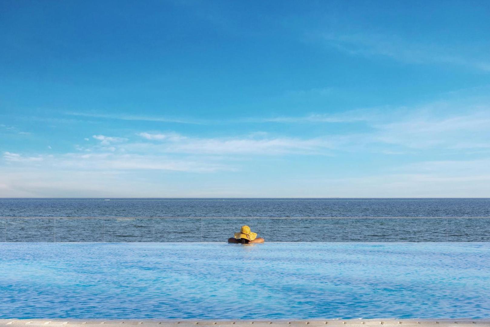Sieviete ar cepuri Bamburi Beach Hotel bezgalības baseinā, raugoties uz zilo Indijas okeānu horizontā