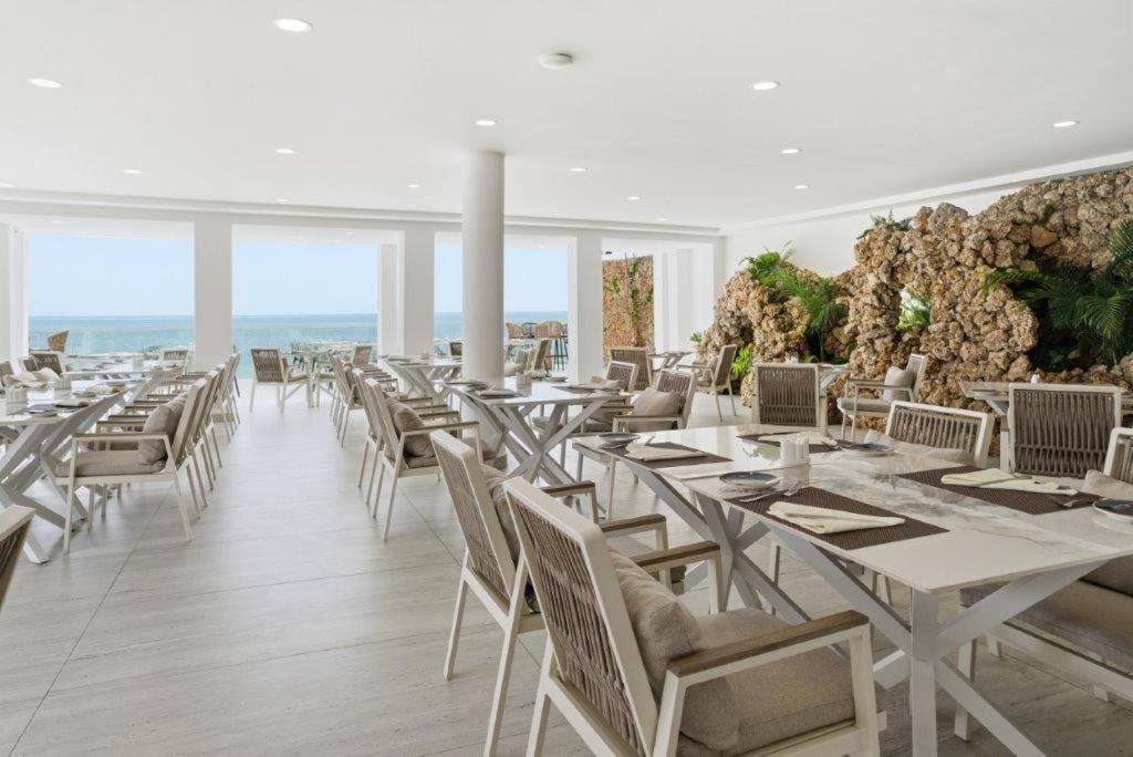 Bamburi Beach Hotel iekštelpu restorāns ar gaišām mēbelēm, dekoratīvu akmens sienu un lieliem logiem uz okeānu.