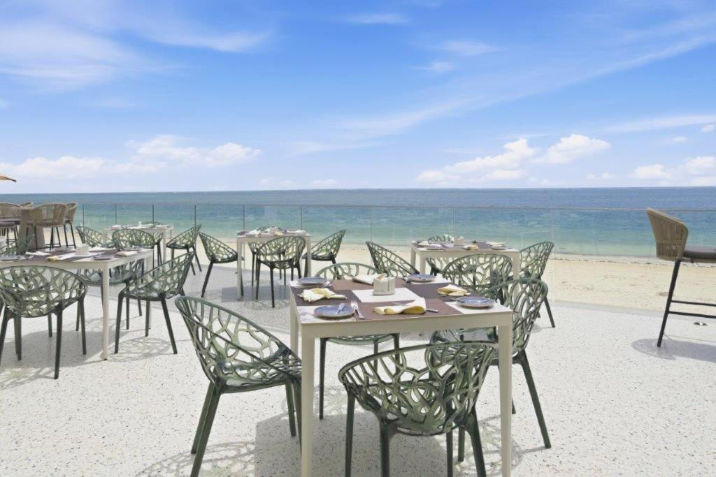 Bamburi Beach Hotel restorāna āra terase ar moderniem galdiem un krēsliem pie okeāna krasta Mombasā, Kenijā — skats uz pludmali