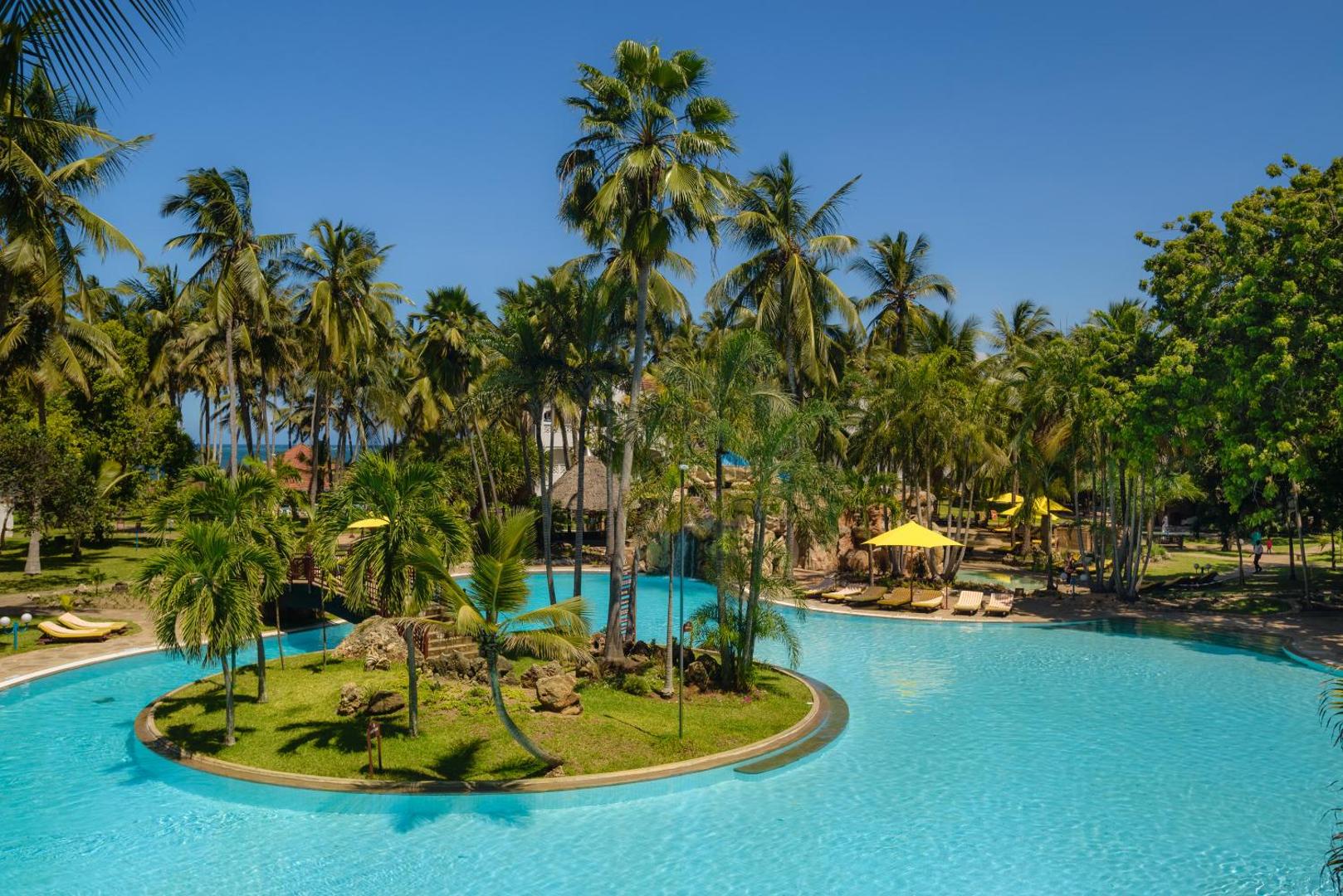 Sarova White Sands Beach Resort & Spa lagūnas tipa baseins ar salu vidū, tiltiņu un augstām palmām saulainā dienā