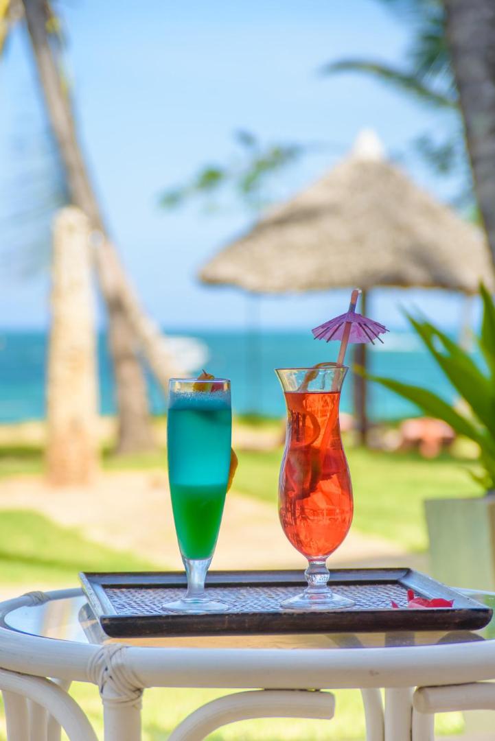 Divi krāsaini tropiskie kokteiļi uz galda Sarova White Sands Beach Resort & Spa pludmales bārā ar okeānu fonā