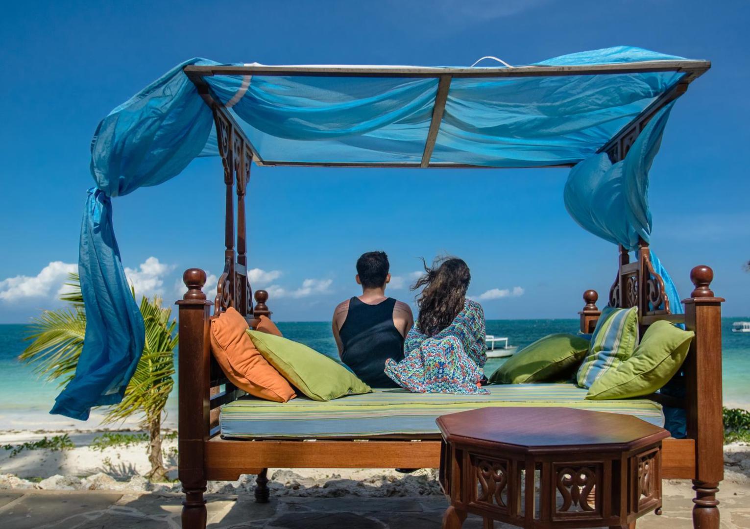 Pāris atpūšas Sarova White Sands Beach Resort & Spa pludmales gultā ar zilu baldahīnu, vērojot tirkīzzilo Indijas okeānu