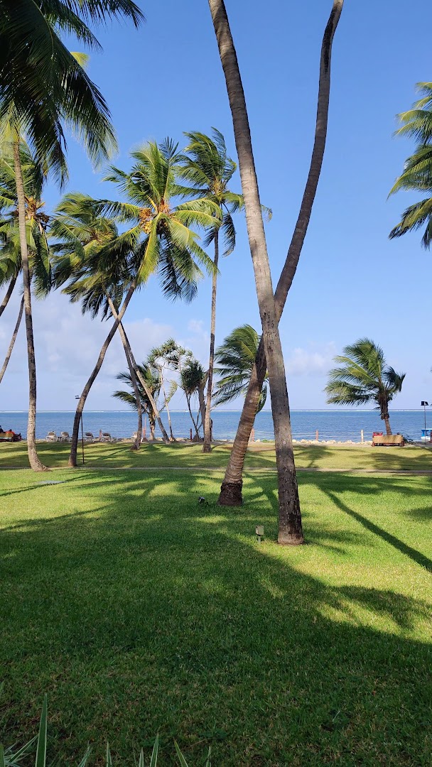 Sarova White Sands Beach Resort & Spa labiekārtots zāliens ar palmām pie okeāna krasta — saulaina diena kūrorta teritorijā Mombasā