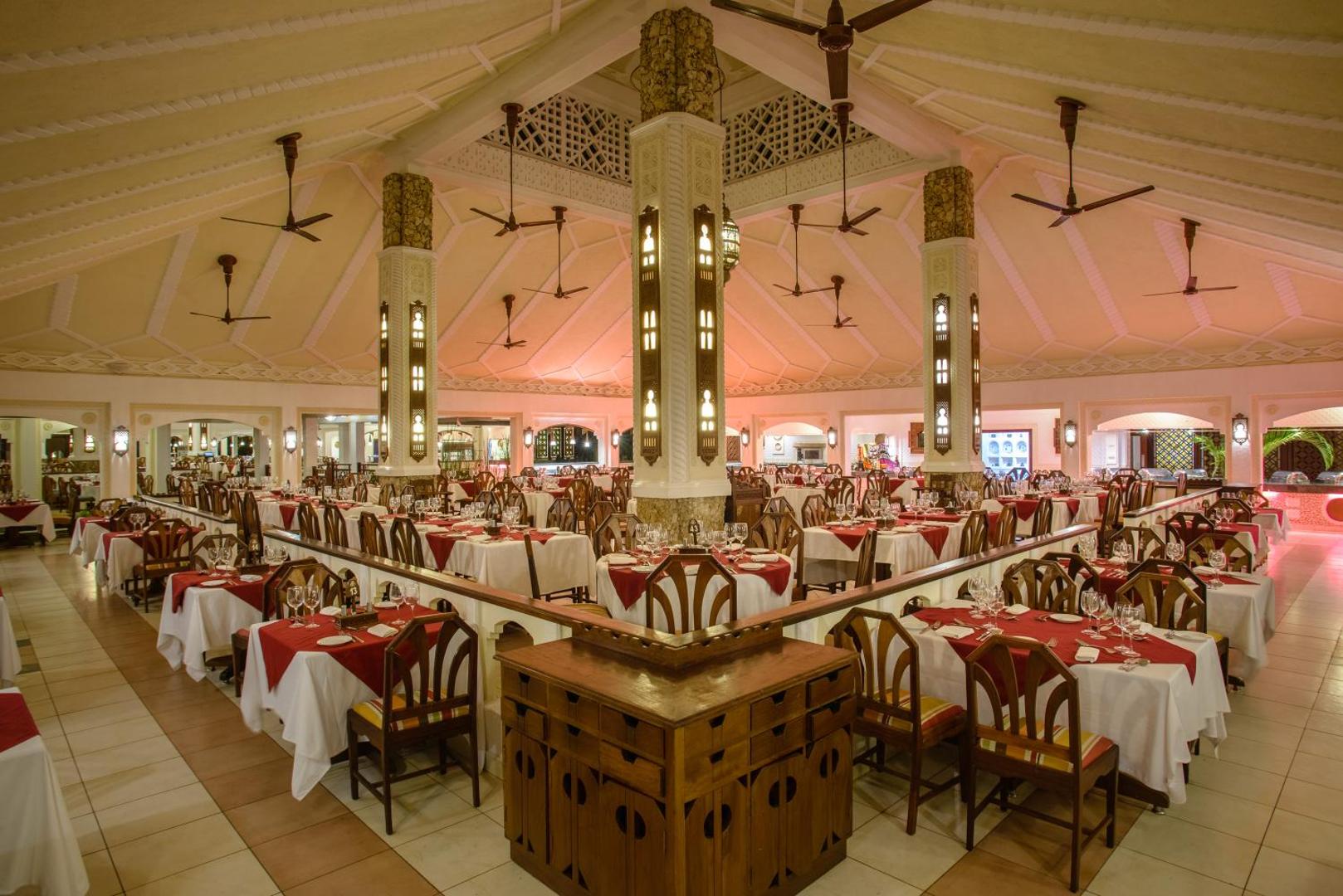 Sarova White Sands Beach Resort & Spa plašā restorāna zāle ar daudziem galdiņiem, koka mēbelēm un dekoratīvām detaļām Kenijā