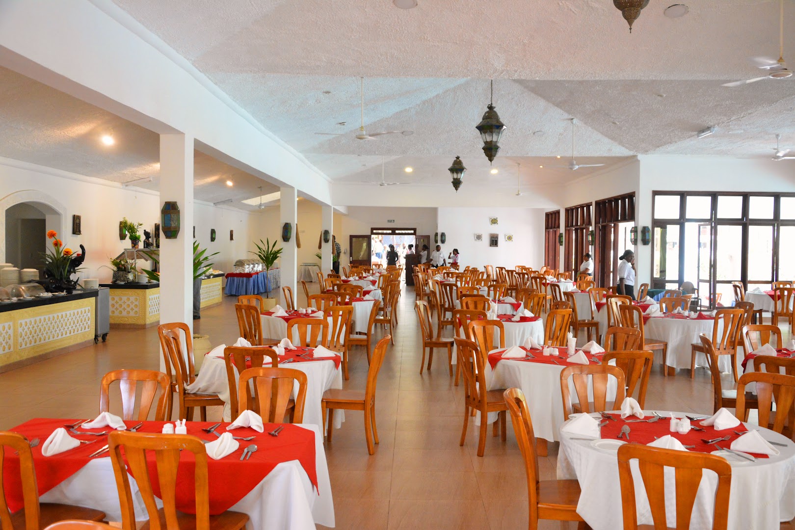 PrideInn Flamingo Beach Resort & Spa plašā restorāna zāle ar balti klātiem galdiem un sarkaniem akcentiem Mombasā