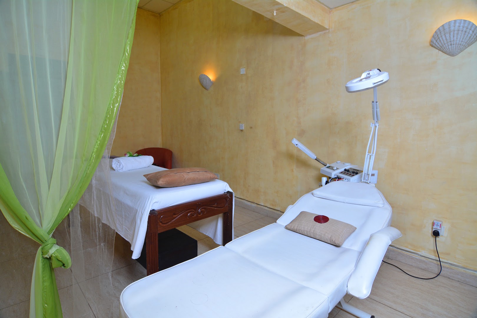 PrideInn Flamingo Beach Resort & Spa procedūru telpa ar divām masāžas gultām, gaišām sienām un zaļiem aizkariem Mombasā, Kenijā
