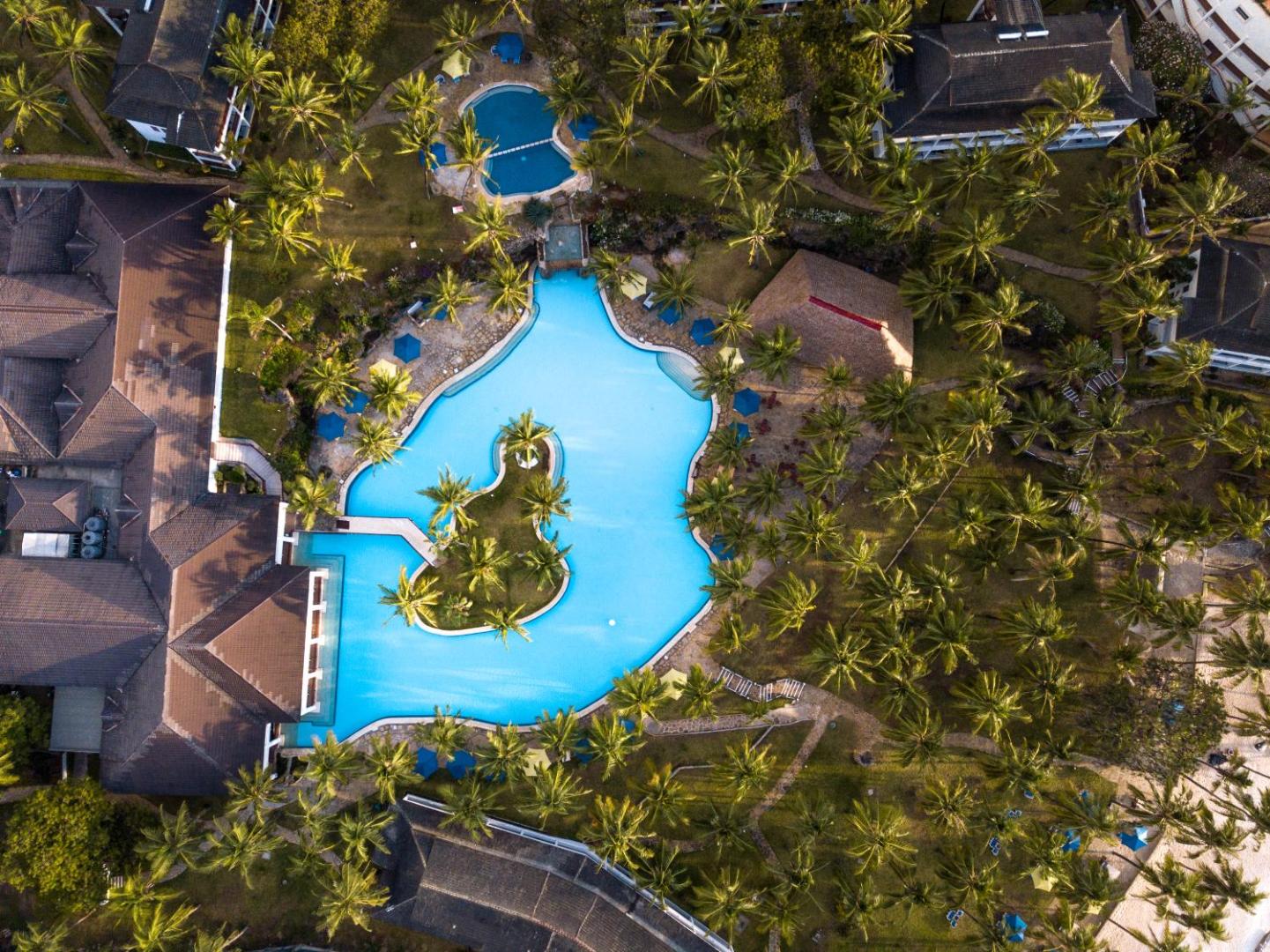 PrideInn Flamingo Beach Resort & Spa skats no augšas uz galveno baseinu, ko ieskauj palmas un viesnīcas ēkas Kenijā