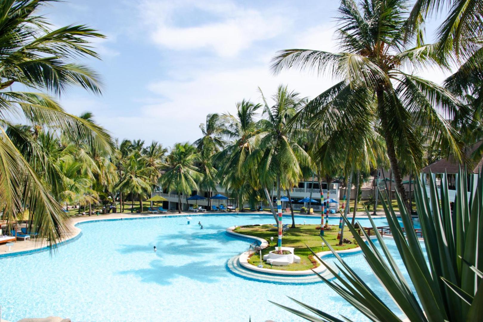 PrideInn Flamingo Beach Resort & Spa lielais peldbaseins ar saulessargiem un palmām — skats no augšējā stāva terases