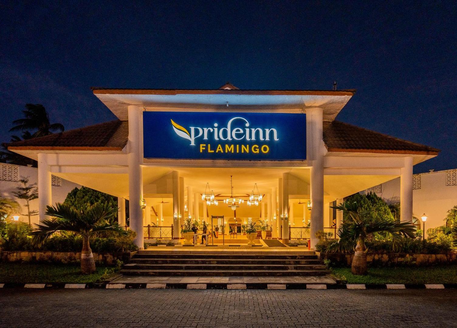 PrideInn Flamingo Beach Resort & Spa galvenā ieeja vakarā ar izgaismotu viesnīcas logo un palmām pie kāpnēm