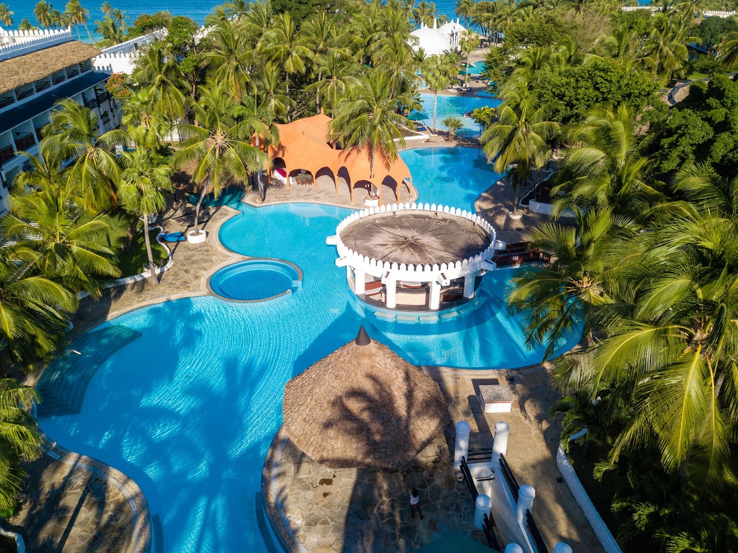 Southern Palms Beach Resort baseina bārs un atpūtas zona ar salmu jumta saulessargiem un eksotisku arhitektūru palmu ielenkumā.