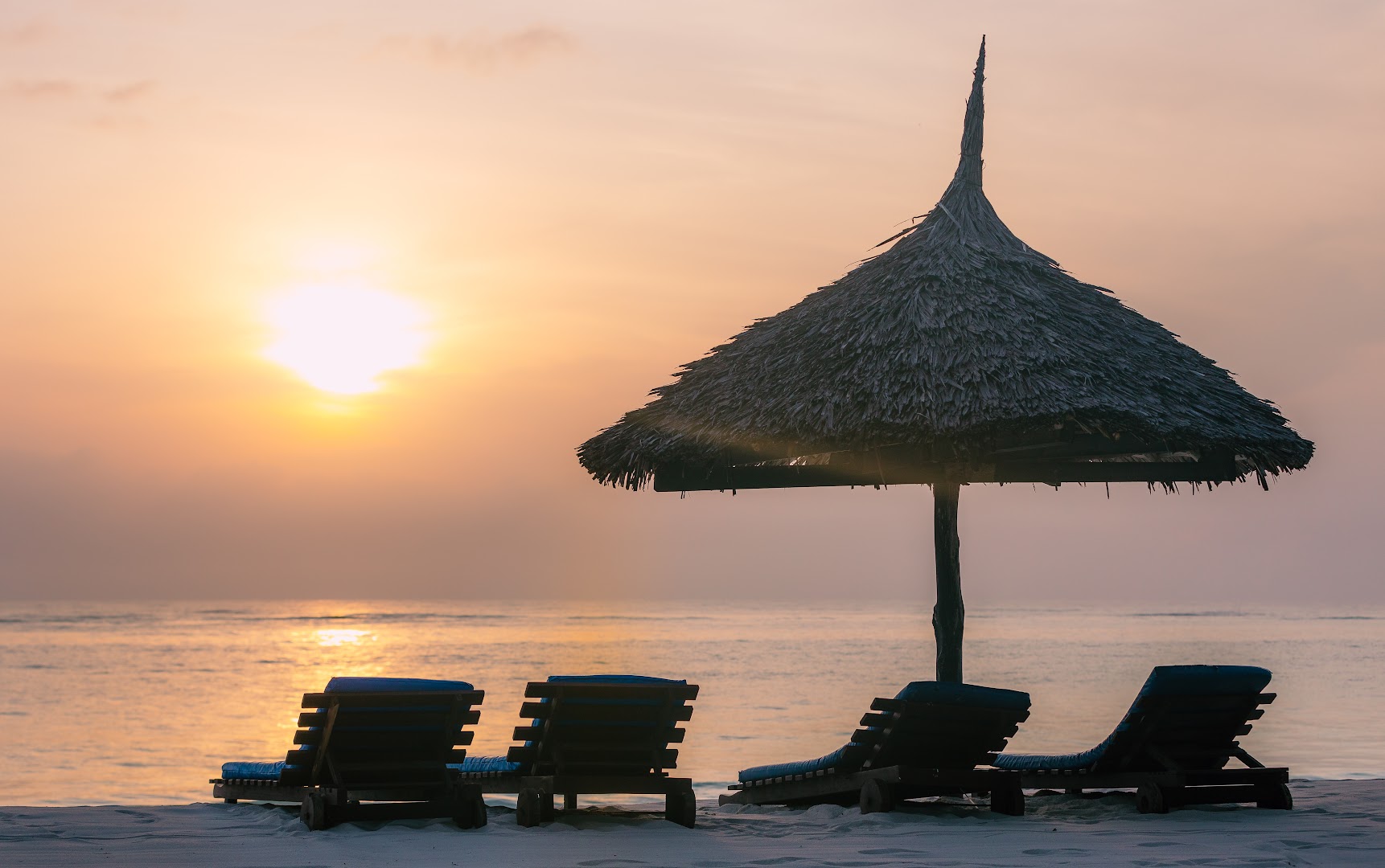 Saulriets Southern Palms Beach Resort pludmalē ar sauļošanās krēsliem un tradicionālu salmu saulessargu pie Indijas okeāna