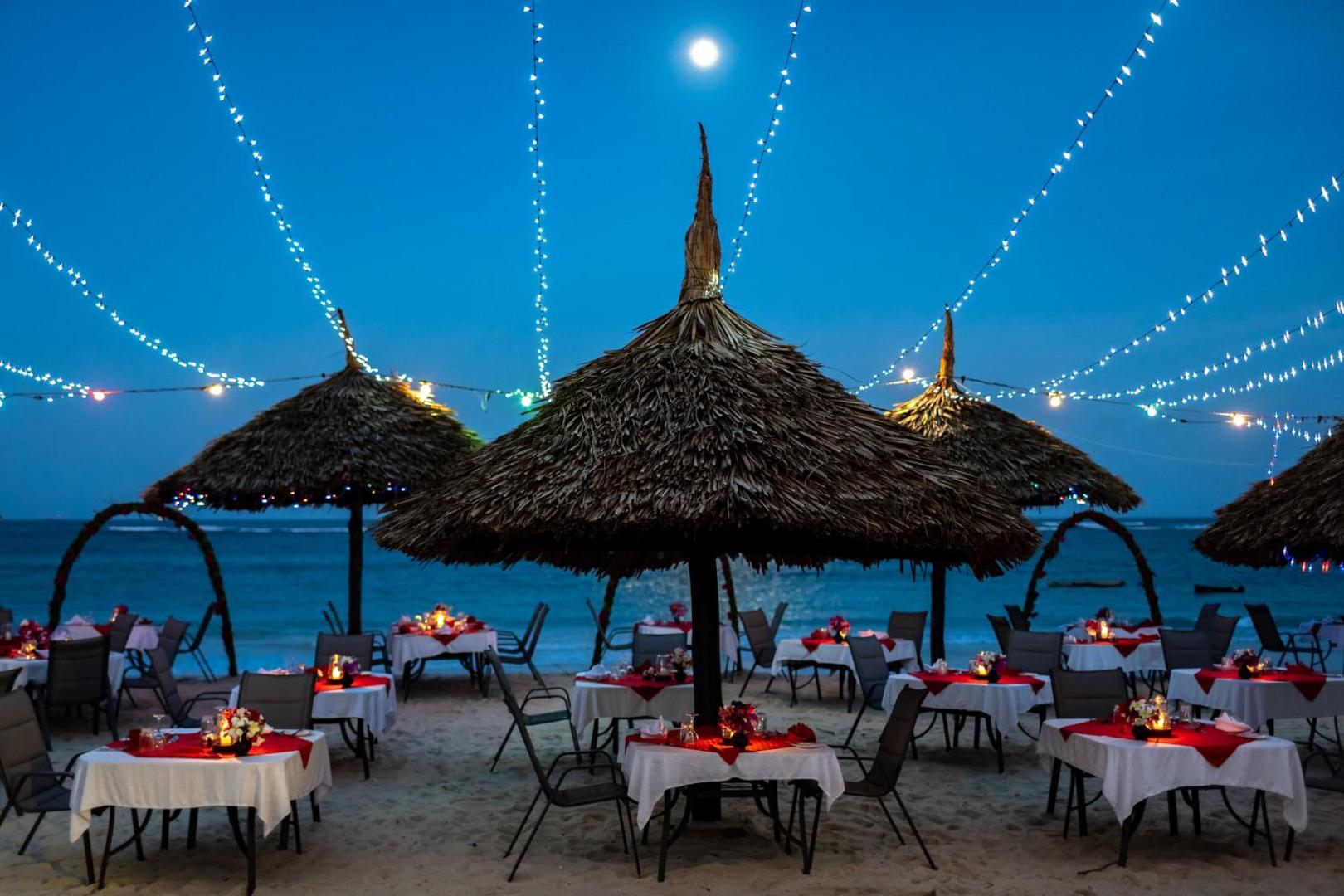 Southern Palms Beach Resort restorāns pludmalē vakarā ar klātiem galdiem zem salmu saulessargiem un dekoratīvām gaismām pie okeāna krasta