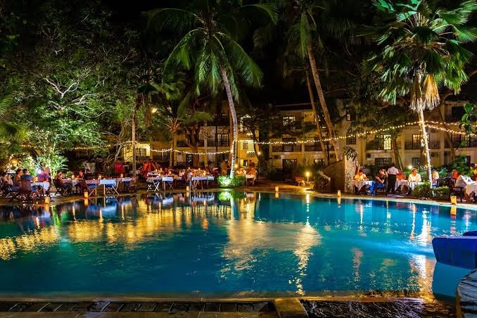 Diani Sea Lodge vakariņas pie izgaismota baseina naktī ar galdiņiem un svētku lampiņām palmās Kenijā
