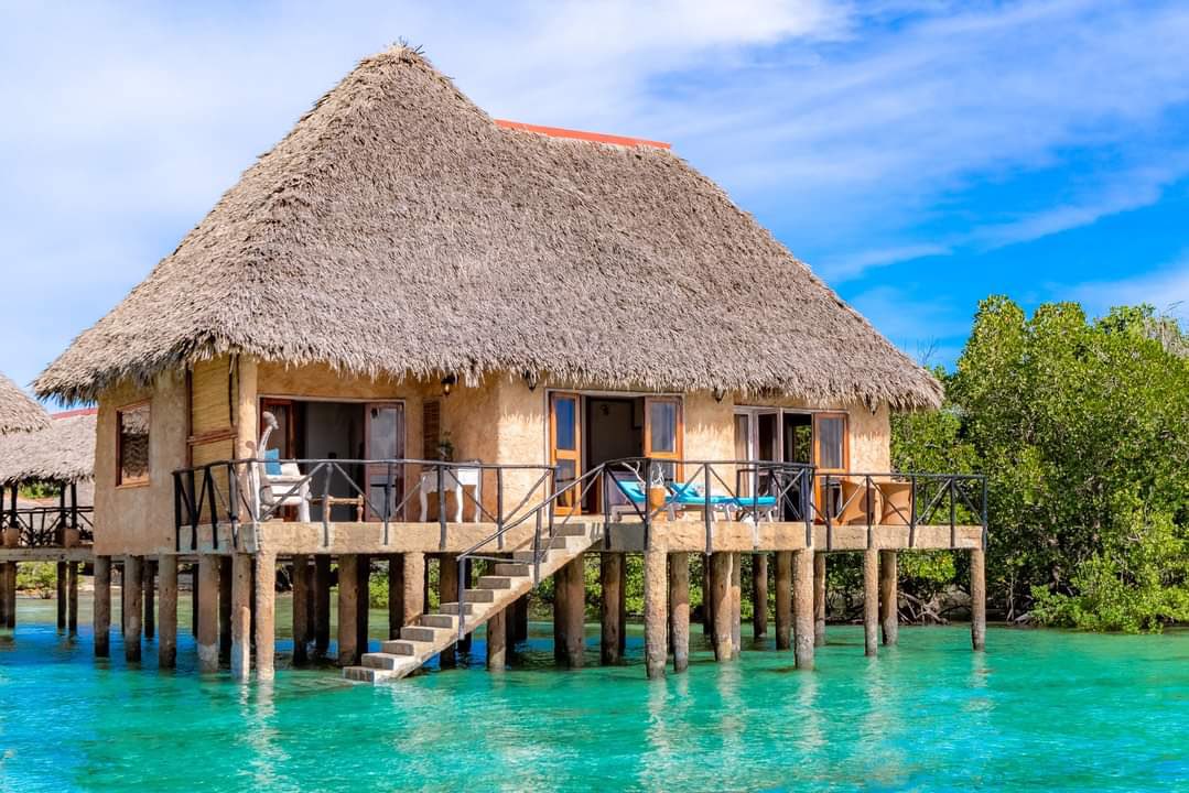 Diani Sea Lodge bungalo uz pāļiem okeāna piekrastē Kenijā — tradicionāls niedru jumts, koka terase un tirkīzzils ūdens