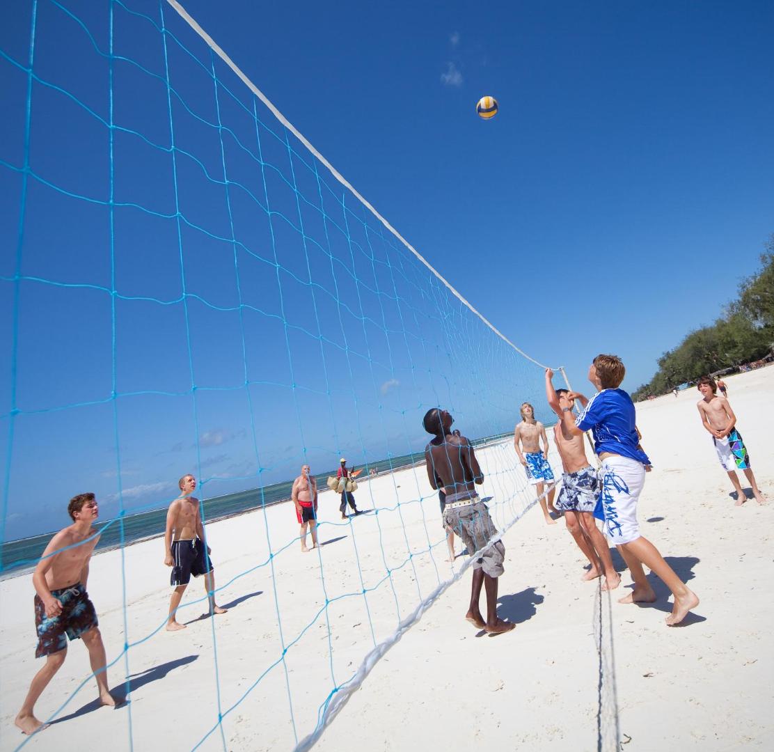 Diani Sea Lodge viesnīcas viesi spēlē pludmales volejbolu piekrastē Kenijā — balto smilšu pludmale un zilas debesis