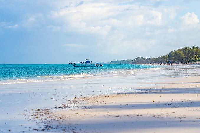 Diani Sea Lodge skats uz plašo Diani pludmali Kenijā ar tirkīzzilu okeāna ūdeni un motorlaivu piekrastē saulainā dienā