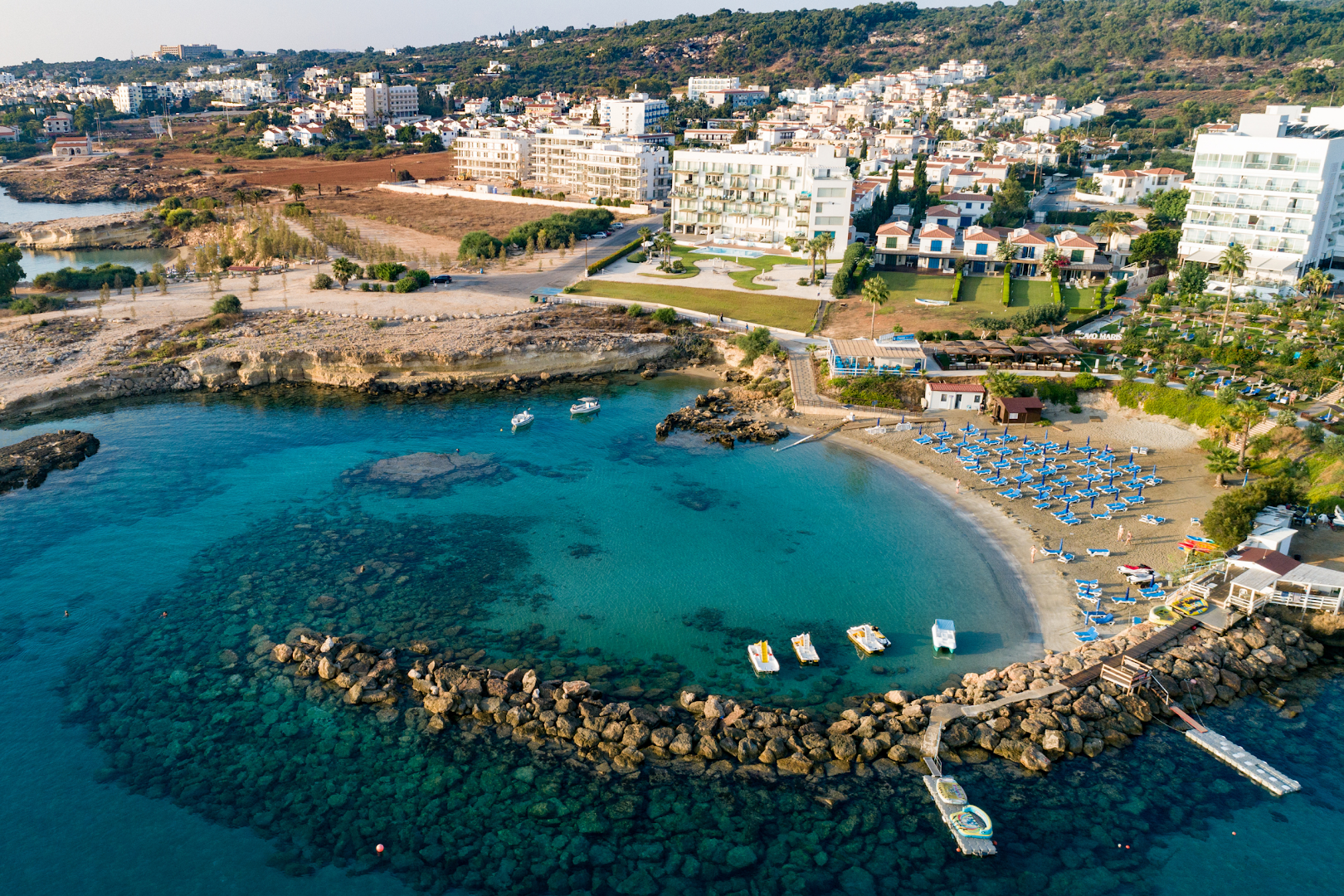 Cavo Maris Beach Hotel privātais līcis ar dzidru tirkīza ūdeni, smilšu pludmali un saulessargiem Protarasas piekrastē