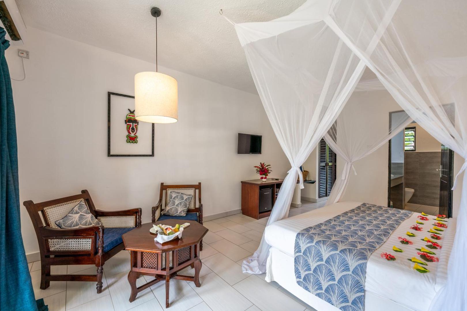 Diani Sea Resort viesnīcas numurs ar dekorētu gultu, koka mēbelēm un tradicionāliem afrikāņu mākslas elementiem pie sienas