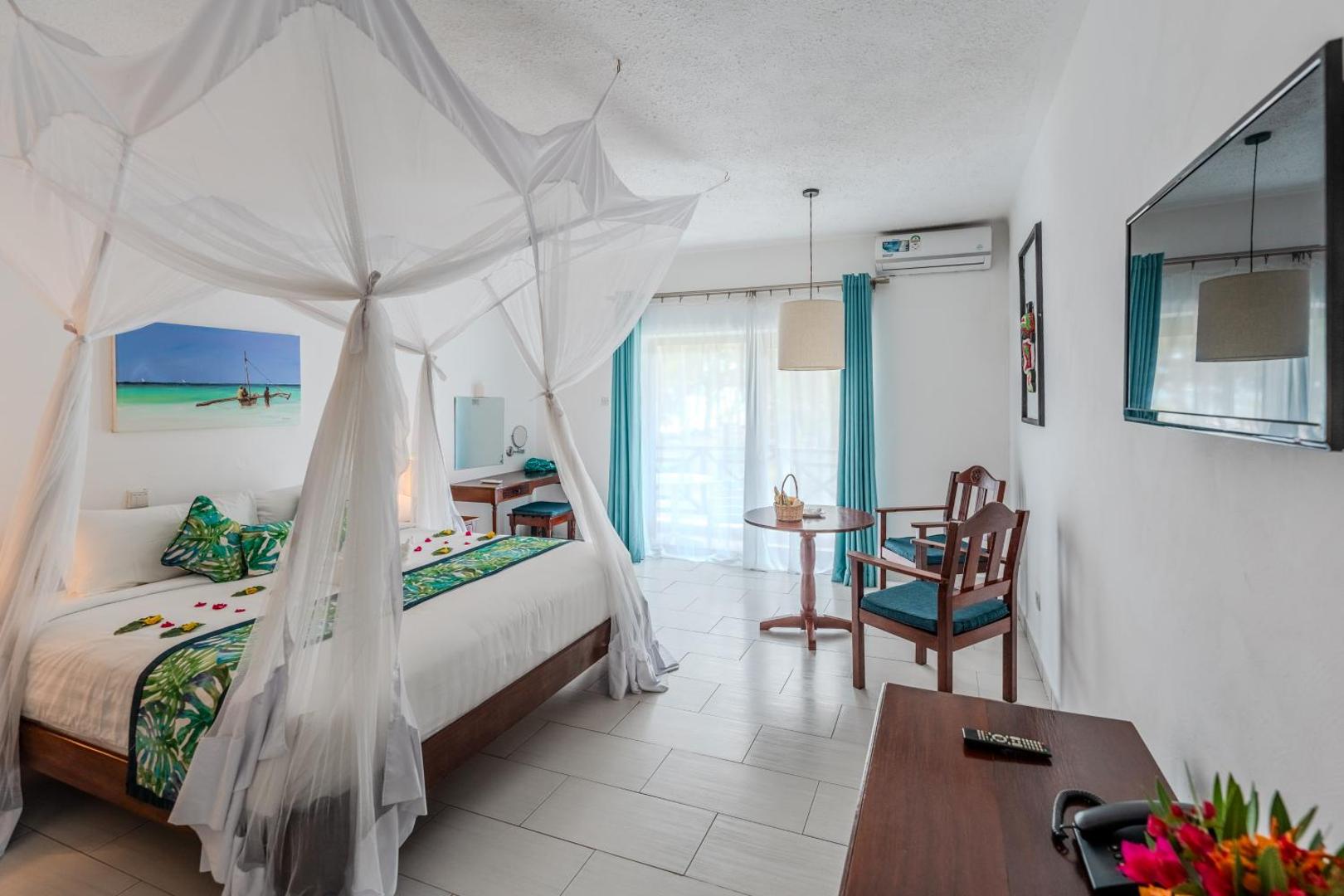 Diani Sea Resort gaišs viesnīcas numurs ar divguļamo gultu, moskītu tīklu un atpūtas zonu pie loga Kenijas piekrastē