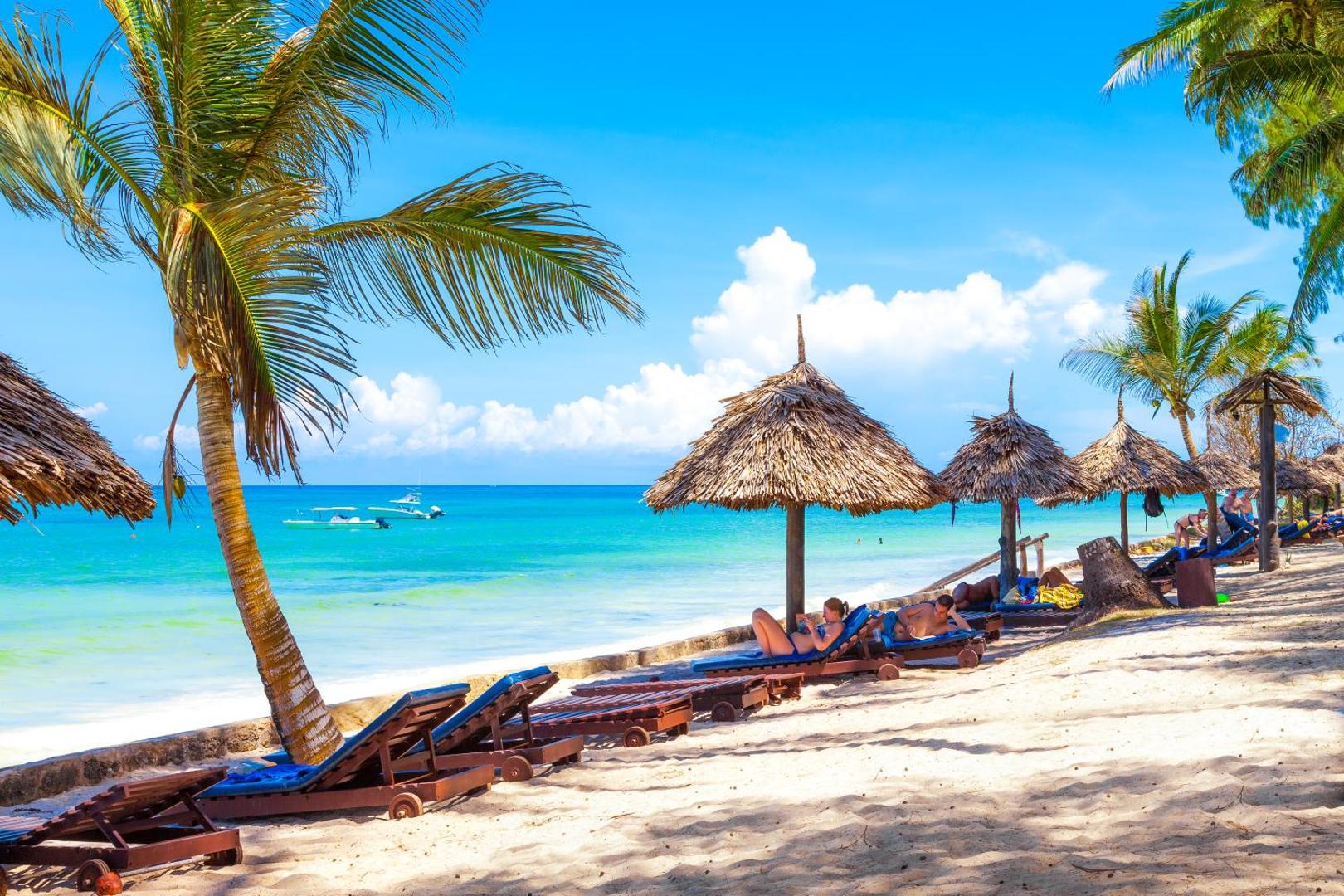 Diani Sea Resort privātā pludmale ar koka sauļošanās krēsliem un salmu saulessargiem pie dzidri zilā Indijas okeāna krasta Kenijā