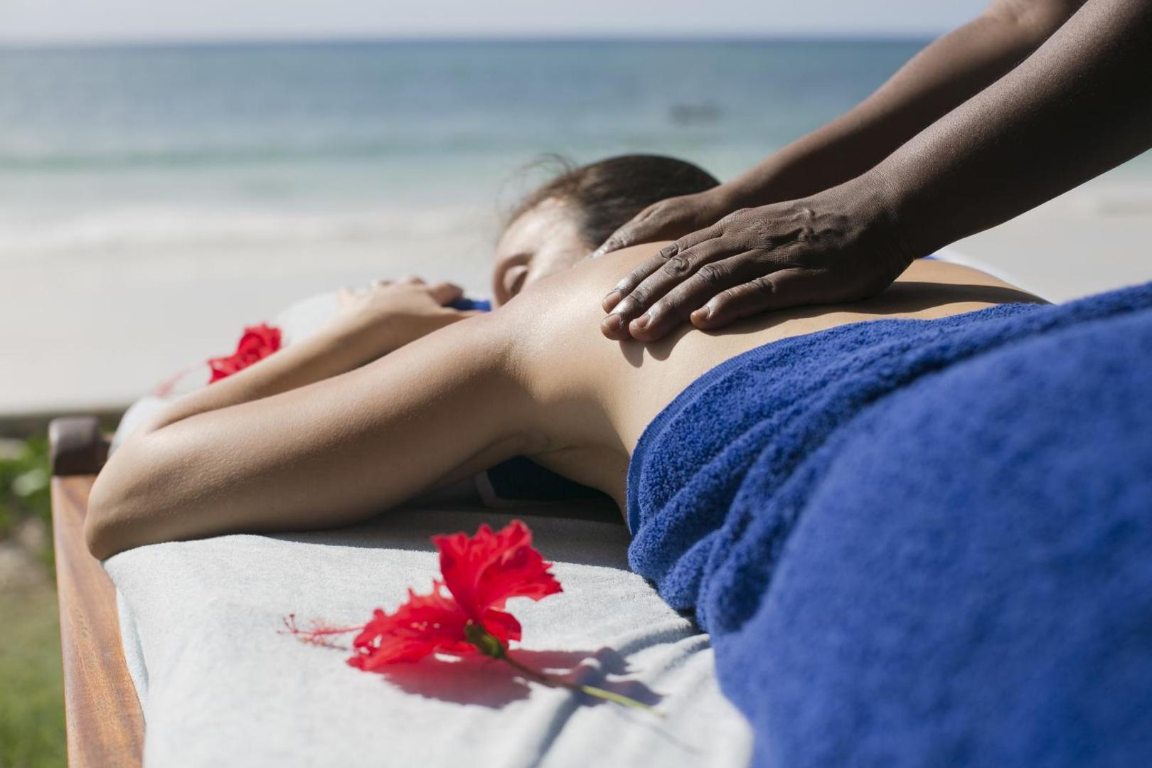 Relaksējoša masāža Diani Sea Resort pludmalē — sieviete bauda spa procedūru pie okeāna ar skatu uz zilo ūdeni