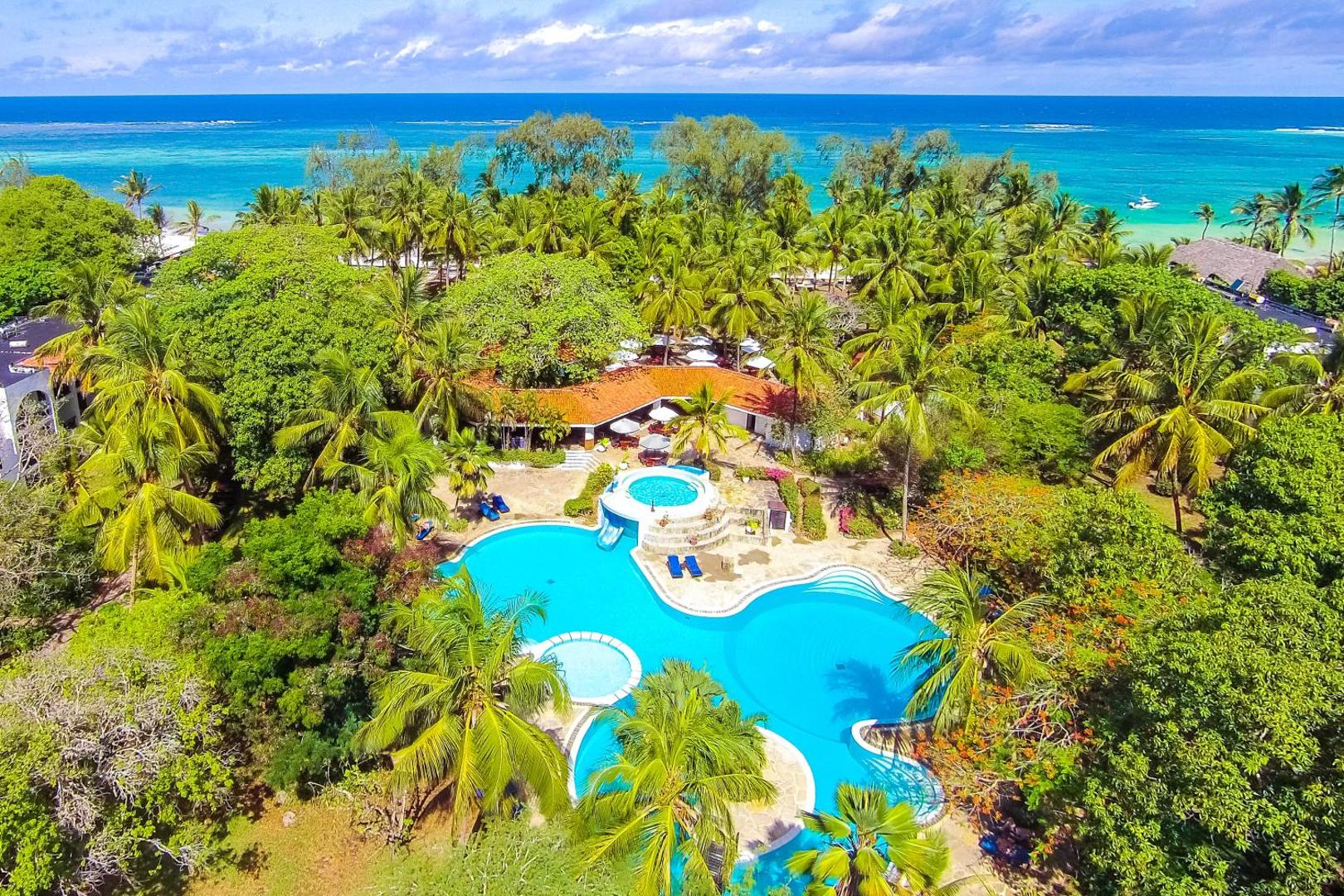 Diani Sea Resort panorāmas skats no putna lidojuma uz āra baseinu kompleksu, apkārtējo palmu dārzu un Indijas okeāna piekrasti Kenijā.