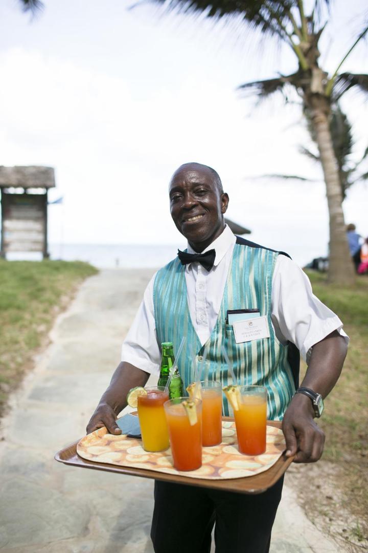 Diani Sea Resort viesmīlis ar paplāti, uz kuras ir tropiskie kokteiļi, uz pludmales takas palmu fonā
