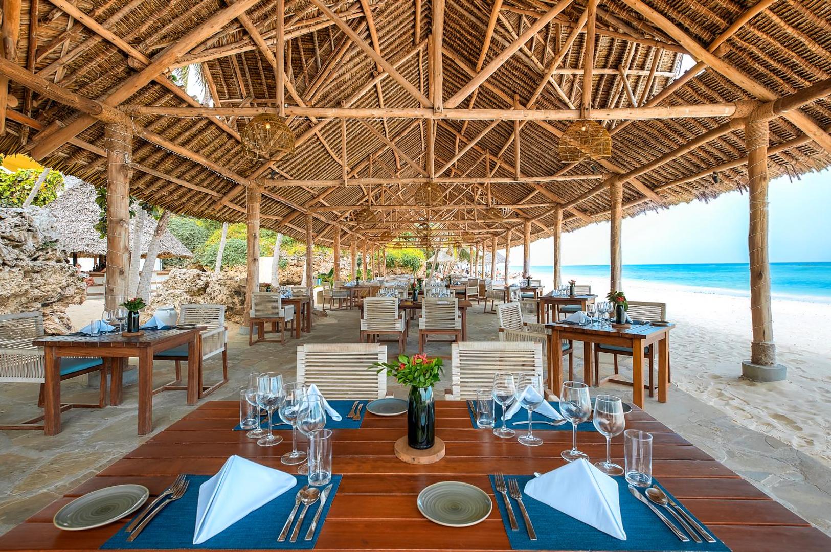 Diamond Leisure Beach & Golf Resort restorāna terase ar koka galdiem un skatu uz Indijas okeānu Zanzibāras piekrastē