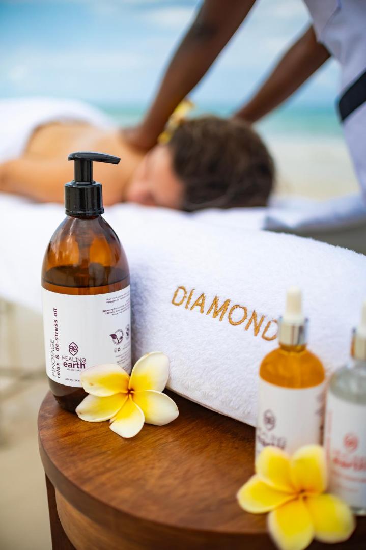 Diamond Leisure Beach & Golf Resort spa procedūra pludmalē ar masāžas eļļām un ziediem uz balta dvieļa fona