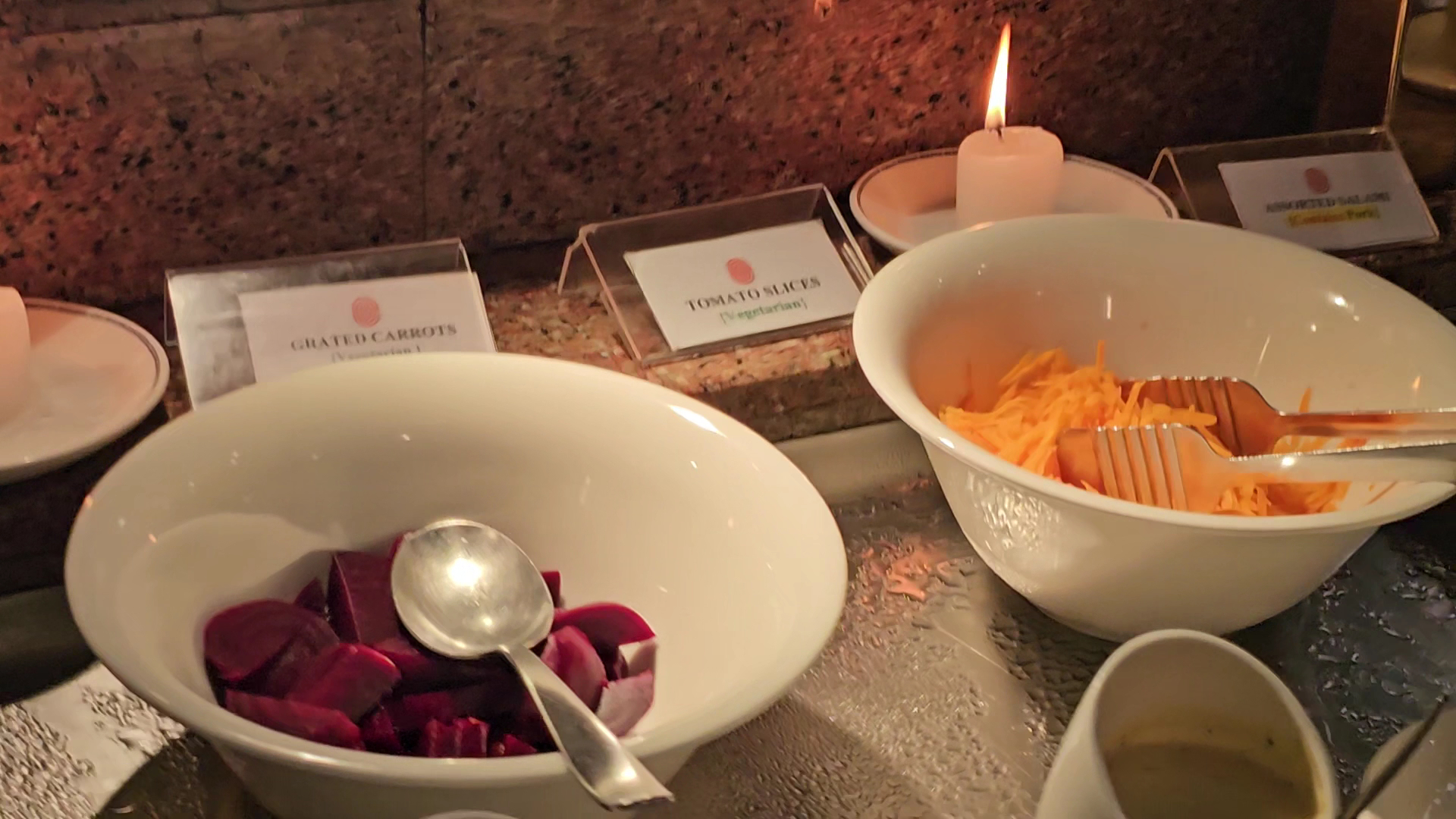 Serena Beach Resort & Spa bufetes galds ar svaigiem salātiem, bietēm un burkāniem, dekorēts ar degošu sveci vakariņu laikā.