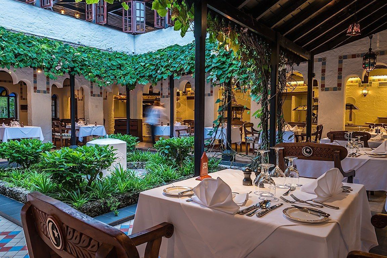 Serena Beach Resort & Spa āra terases restorāns iekšpagalmā ar zaļumiem, vīnogulājiem un eleganti klātiem galdiem piekrastē