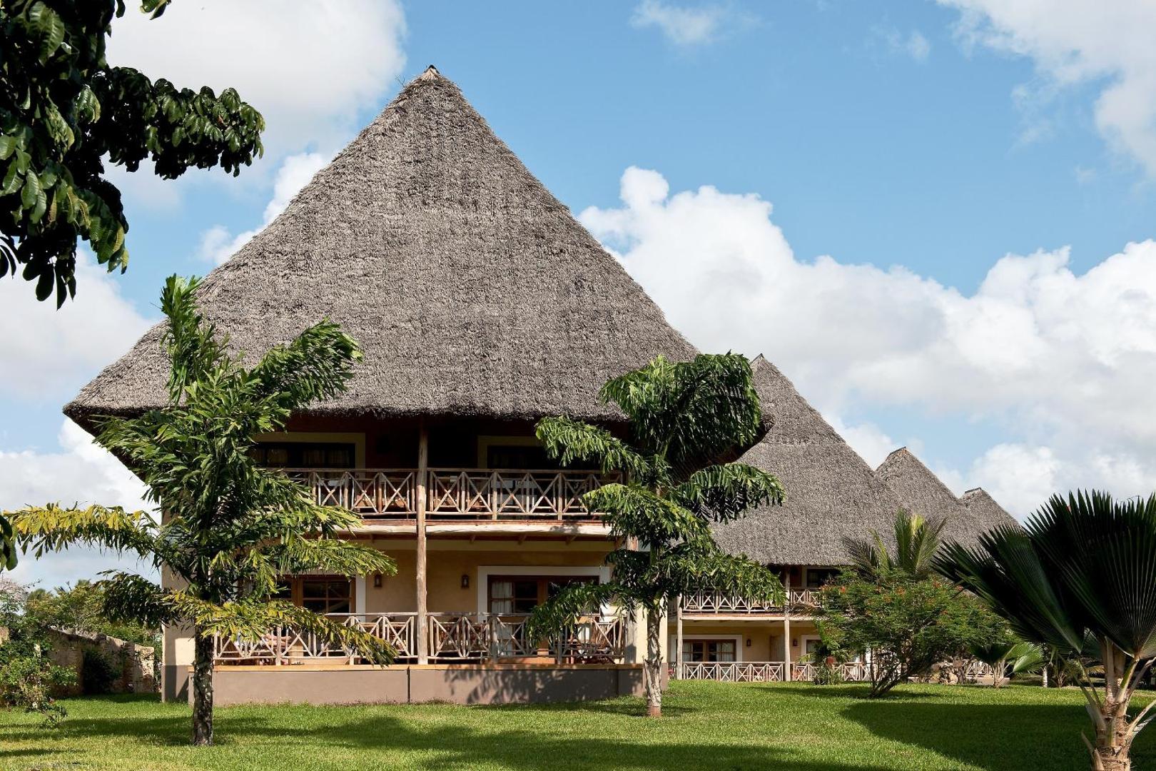 Neptune Palm Beach Boutique Resort & Spa divstāvu bungalo ar tradicionāliem makuti niedru jumtiem un koka balkoniem zaļā dārzā