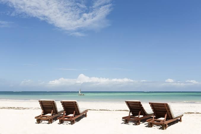 Koka sauļošanās krēsli baltu smilšu pludmalē pie Neptune Palm Beach Boutique Resort & Spa ar skatu uz tirkīza okeānu