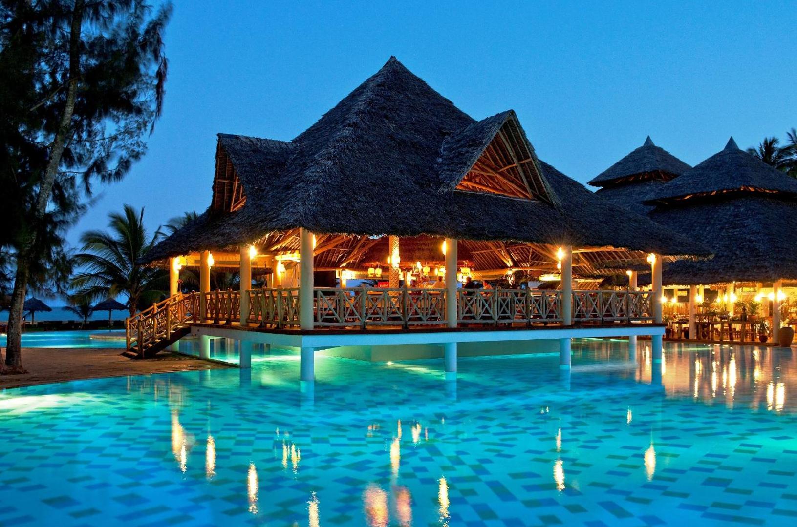 Neptune Palm Beach Boutique Resort & Spa āra baseins un restorāns ar salmu jumtu vakarā, Kenijas piekrastē — izgaismota atpūtas zona