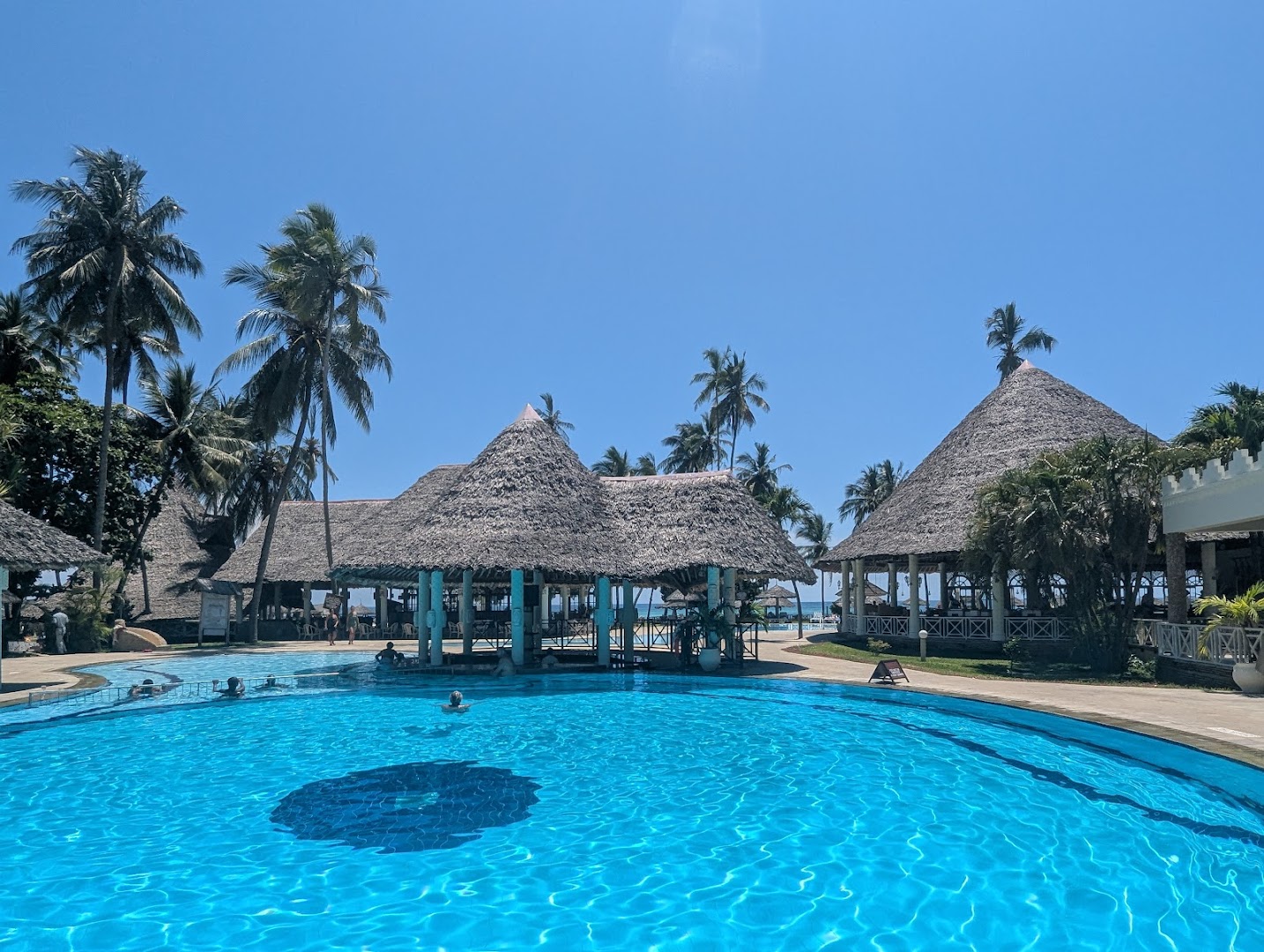 Neptune Palm Beach Boutique Resort & Spa plašais āra baseins saulainā dienā ar bāru un palmām Kenijas kūrortā
