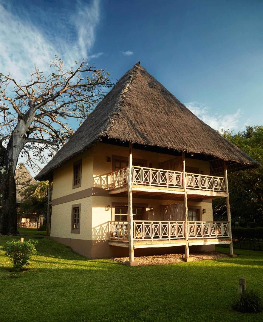 Neptune Palm Beach Boutique Resort & Spa bungalo ēka saulrietā ar koka terasēm un raksturīgo augsto niedru jumtu