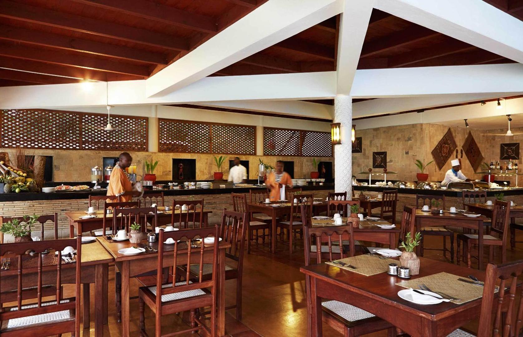 Neptune Palm Beach Boutique Resort & Spa restorāna interjers ar koka mēbelēm un bufetes zonu Zanzibāras boutique viesnīcā.