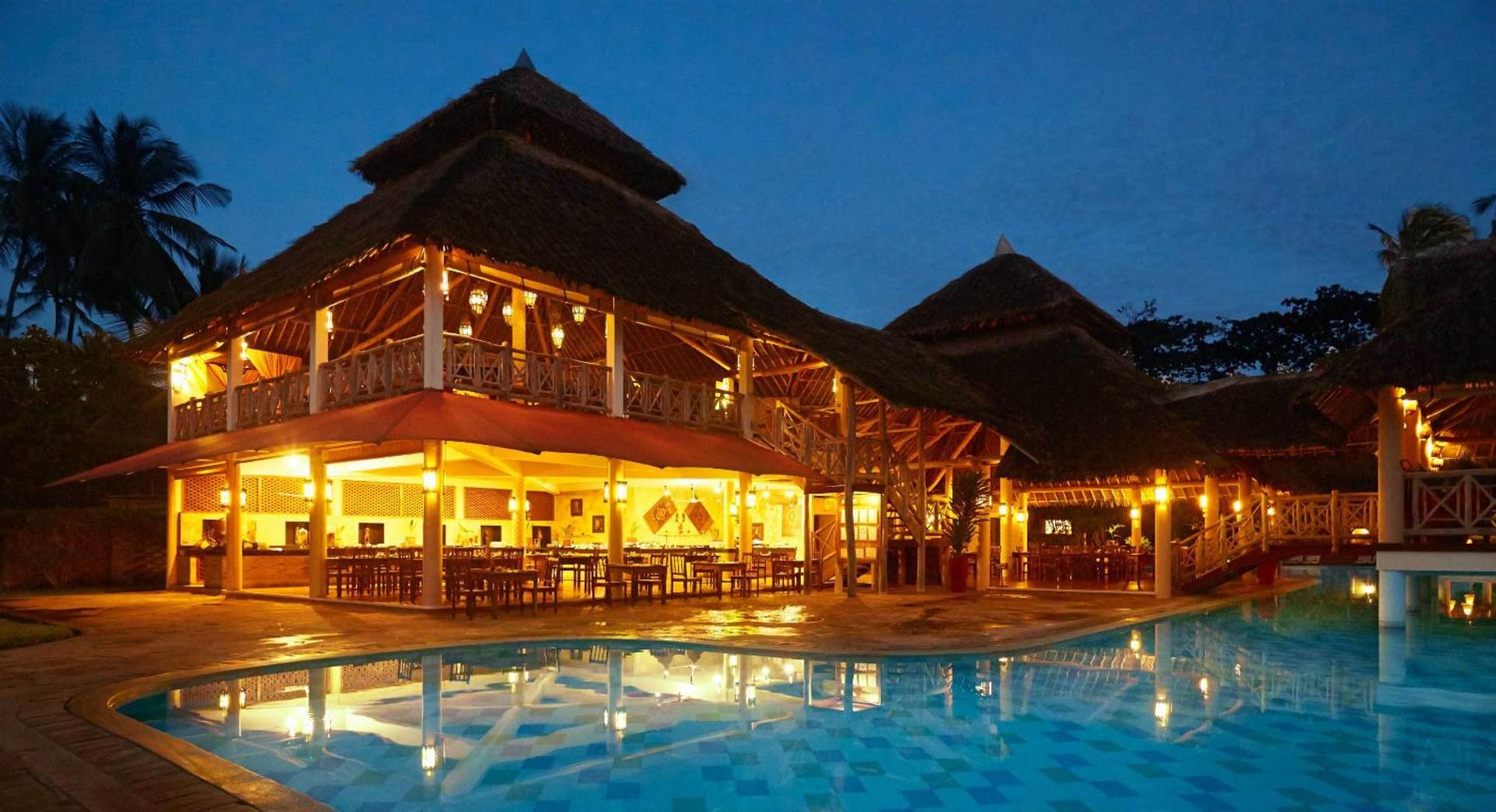 Neptune Palm Beach Boutique Resort & Spa vakara apgaismojums pie āra baseina un galvenās ēkas ar salmu jumtu Zanzibārā.