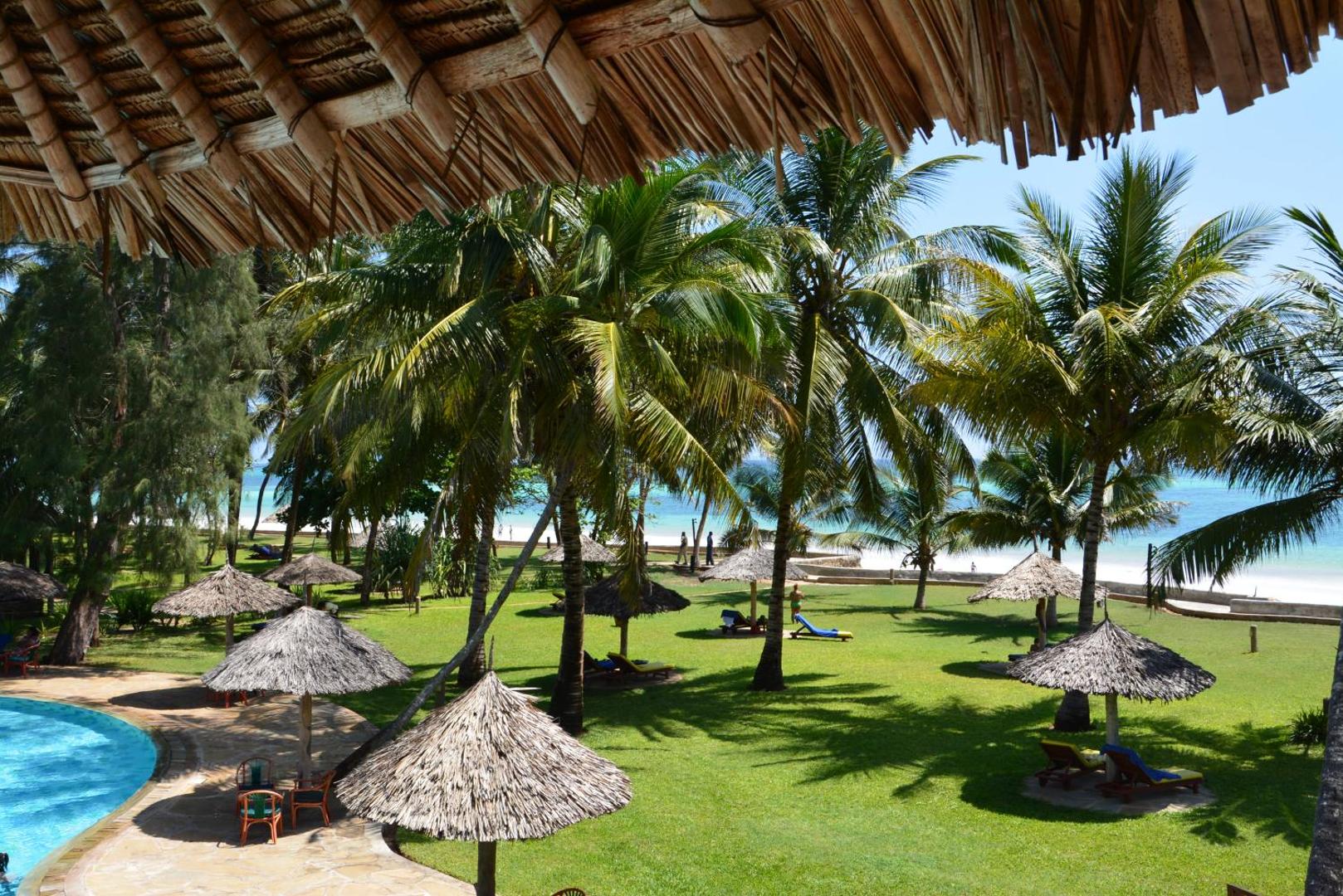 Neptune Palm Beach Boutique Resort & Spa zaļā teritorija ar palmām, zālāju, saulessargiem un baseina malu pie okeāna krasta