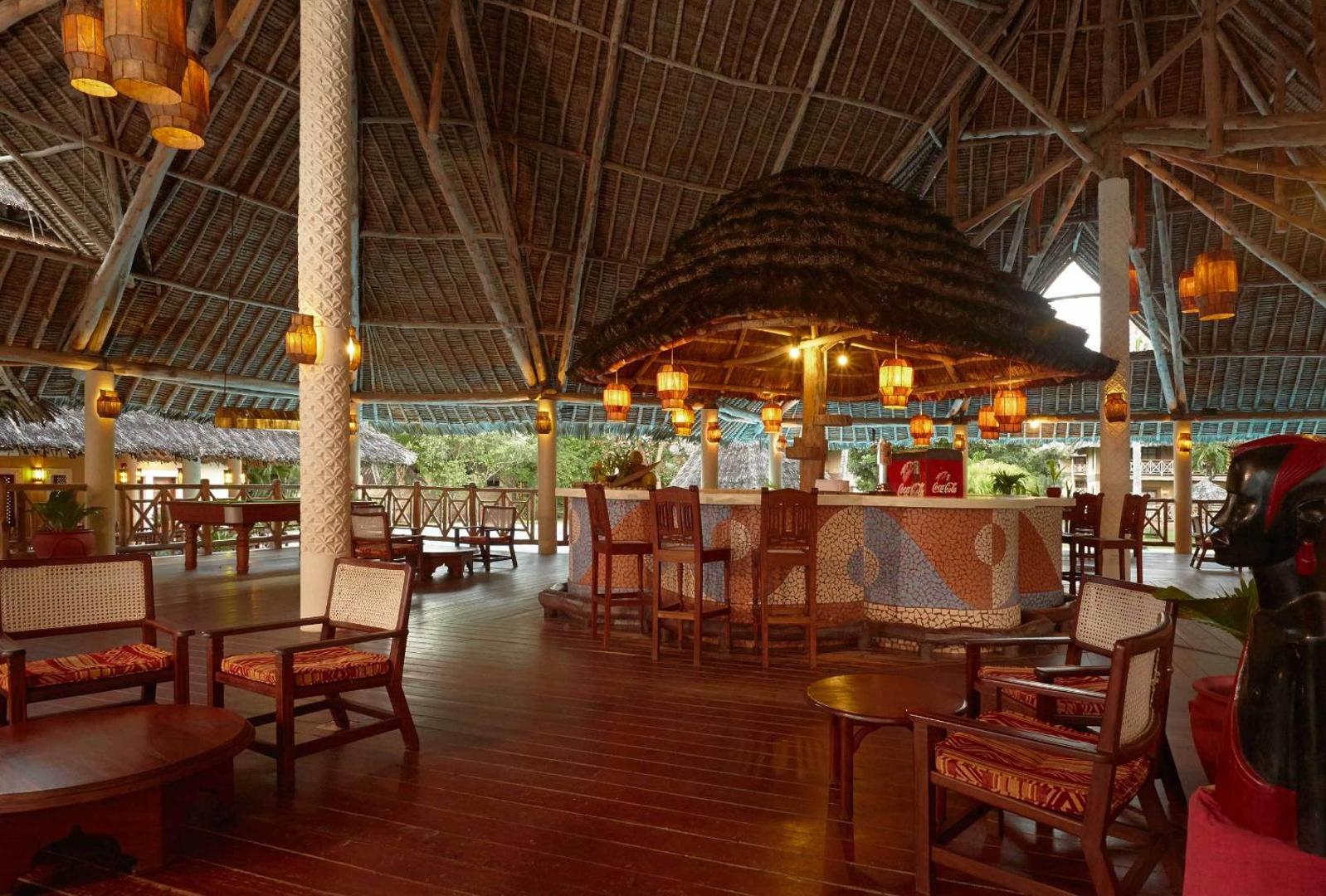 Neptune Palm Beach Boutique Resort & Spa bārs zem augsta niedru jumta ar mozaīkas apdari un mīkstiem krēsliem
