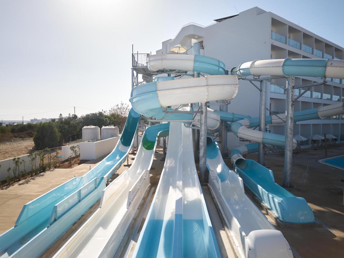 Maris Grand Waterpark Resort ūdens atrakciju parks ar vairākiem paralēliem slidkalniņiem un zili baltām caurulēm pie viesnīcas korpusa Kiprā