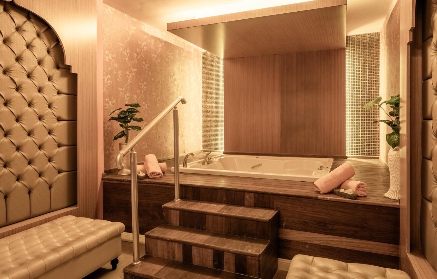 Adalya Bliss spa zonas džakuzi vanna ar koka apdari, mīkstiem soliem un rozā dvieļiem relaksējošā apgaismojumā