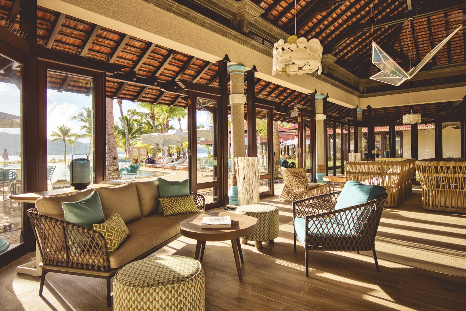 Club Med Seychelles viesnīcas lobby atpūtas zona ar stilīgām mēbelēm, pītiem krēsliem un skatu uz āra baseinu un palmām