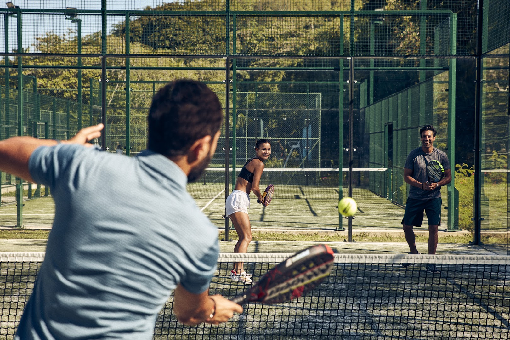 Viesi spēlē padelu Club Med Seychelles sporta laukumā, ko ieskauj zaļi pakalni un tropu veģetācija
