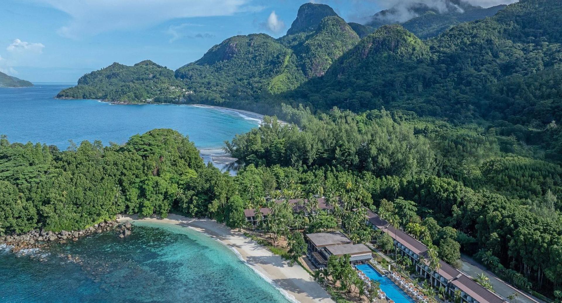 Avani+ Barbarons Seychelles Resort skats no putna lidojuma uz balto smilšu pludmali, tirkīzzilo okeānu un tropu mežu ieskautajām ēkām