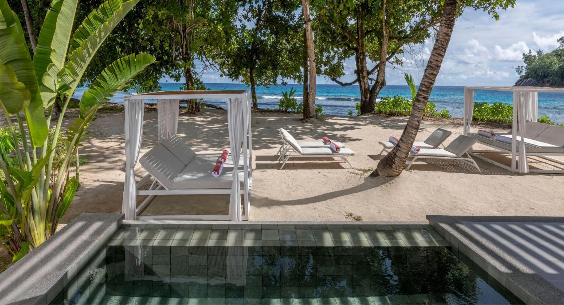 Avani+ Barbarons Seychelles atpūtas zona pludmales smiltīs ar ērtiem zviļņiem un nojumēm — skats uz okeānu caur palmu lapām