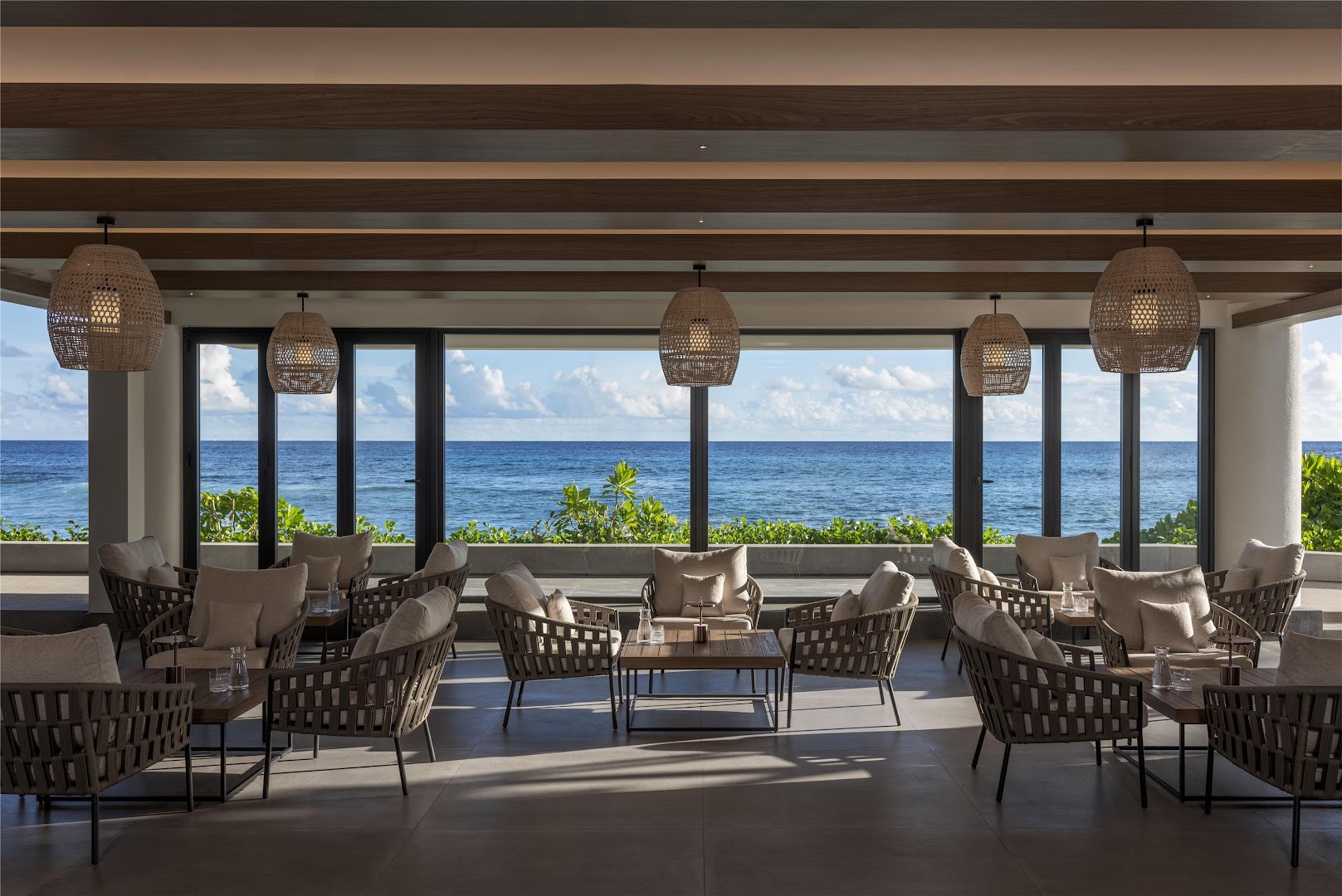 Avani+ Barbarons Seychelles restorāna terase ar pītiem krēsliem, koka galdiem un panorāmas skatu uz Indijas okeānu Seišelu salās