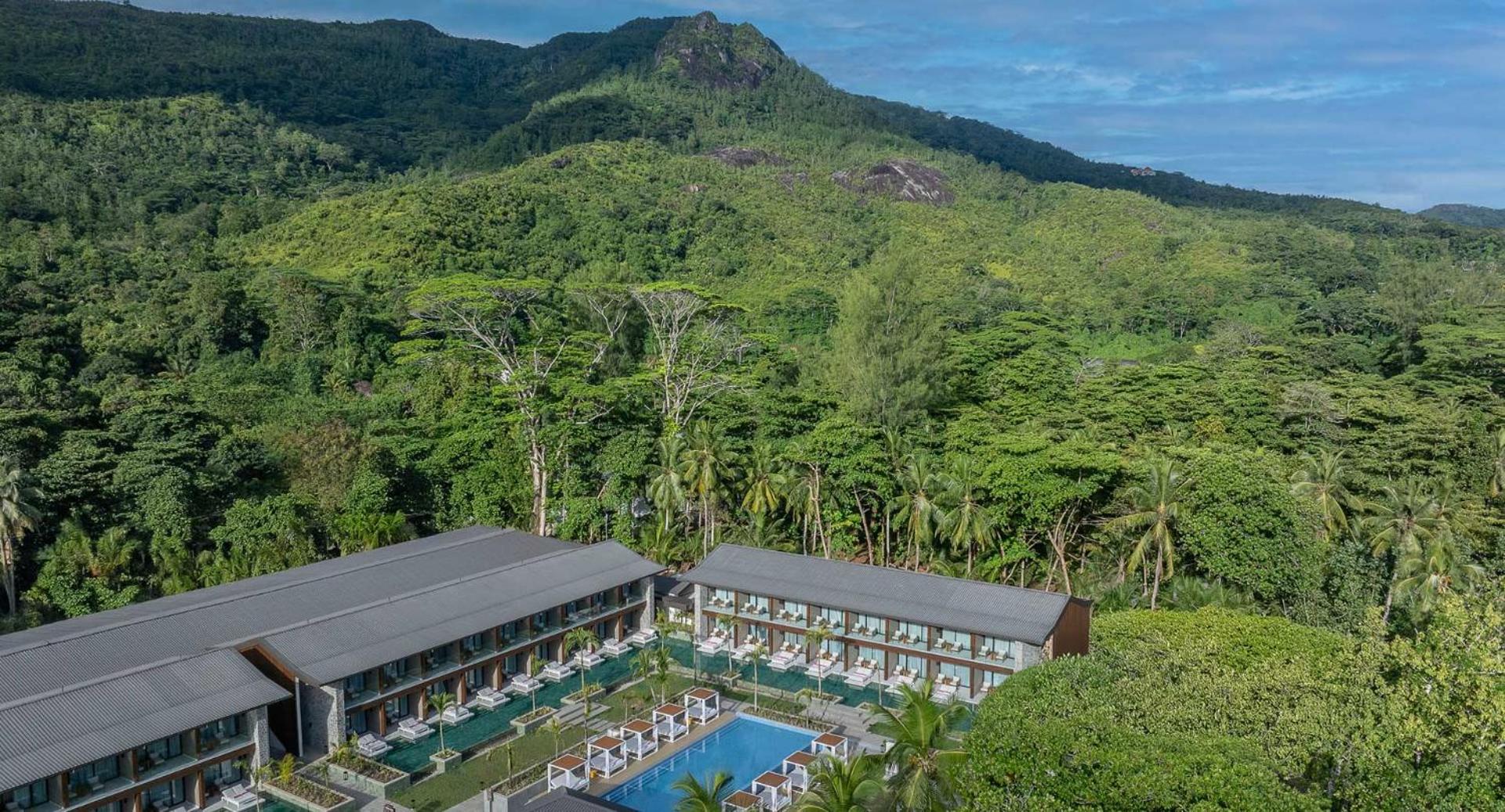 Avani+ Barbarons Seychelles numuru korpusi ar balkoniem un peldbaseinu, fonā redzami zaļojoši kalni un tropu veģetācija